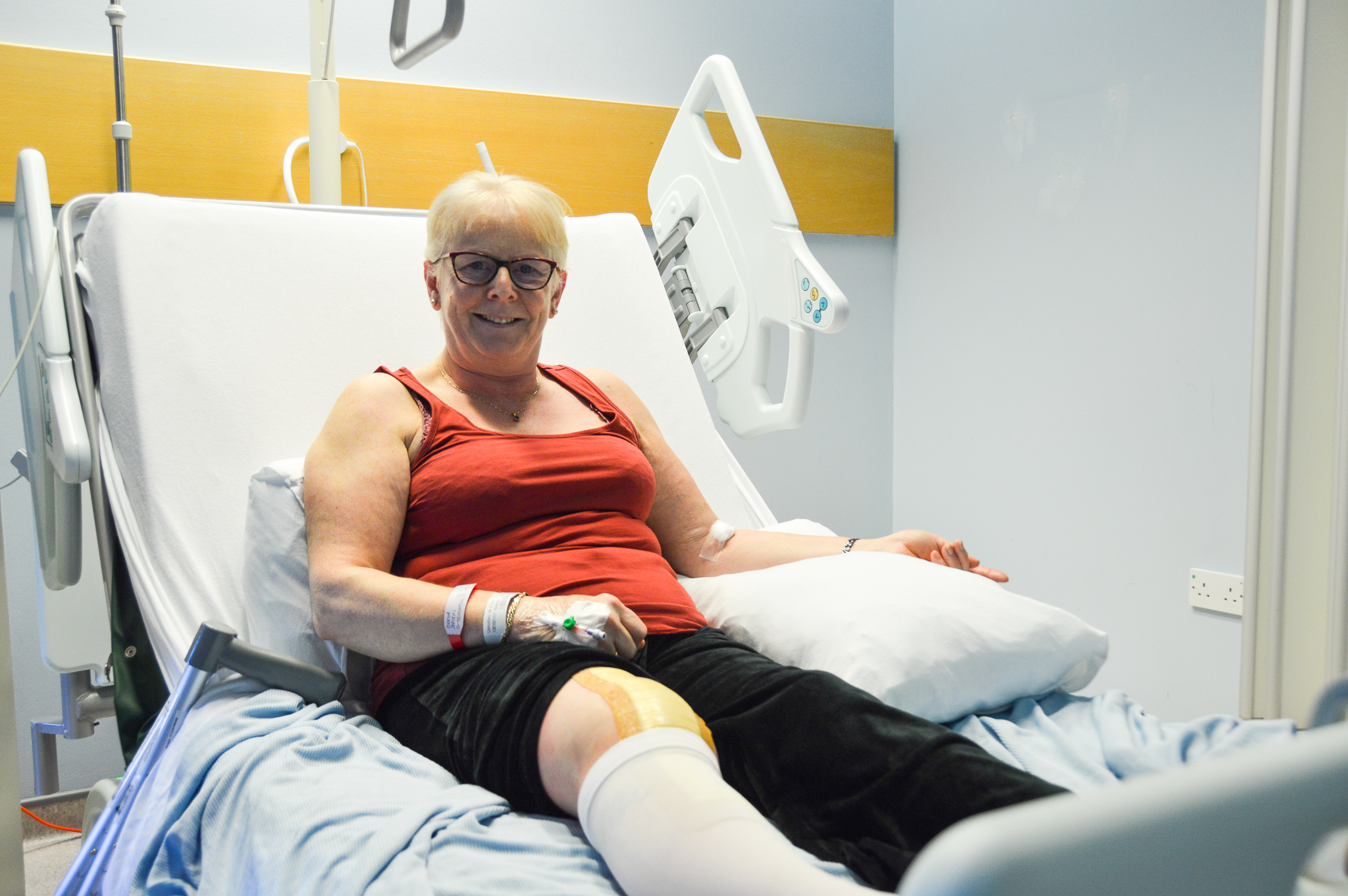 Female patient smiling whilst sitting on hospital bed wearing ankle compression socks.