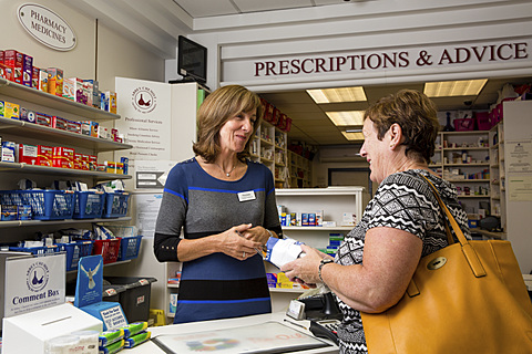 Female pharmacist giving woman prescription and smiling.