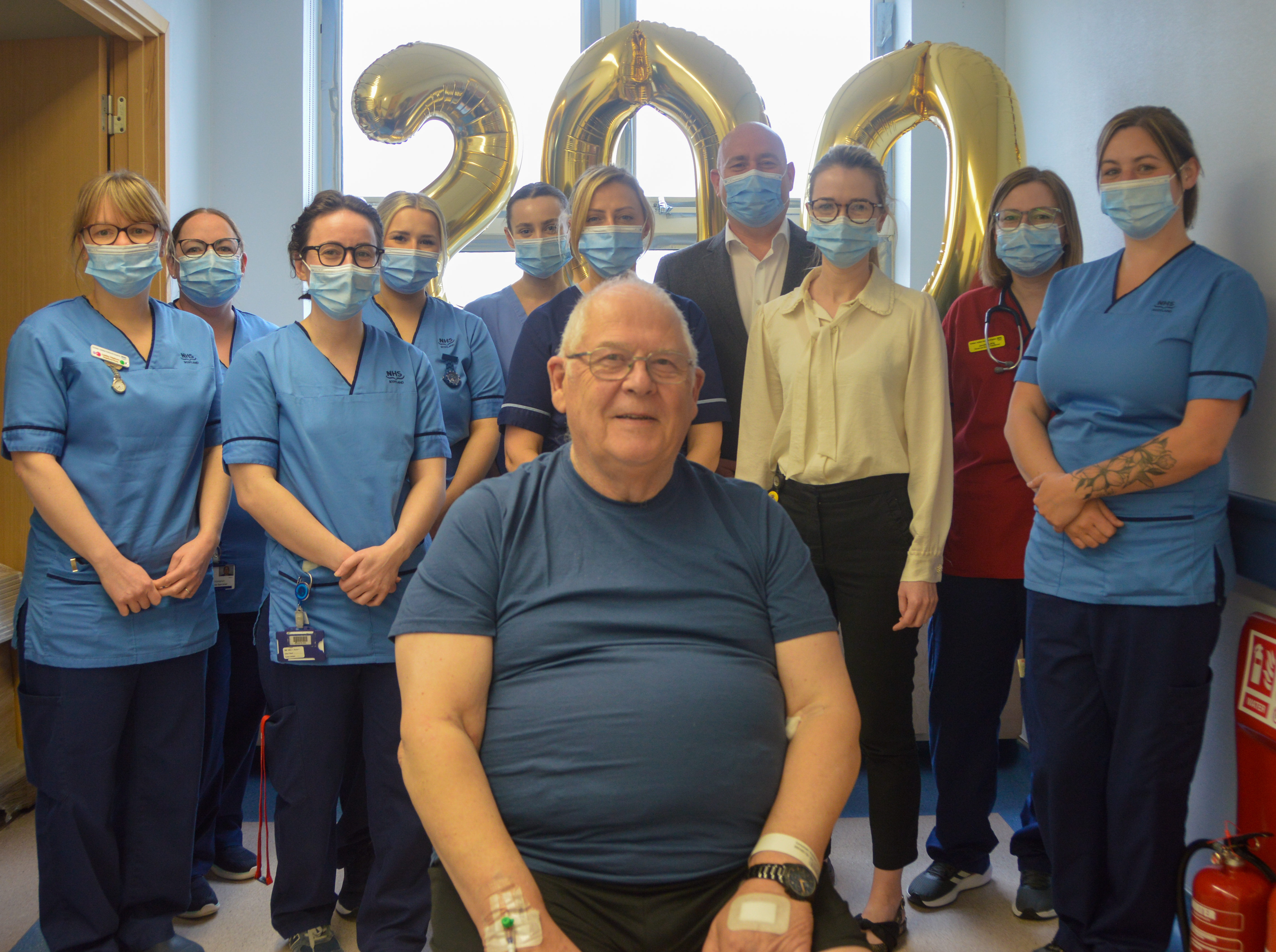 Patient sitting in front of Colorectal Team, with balloons reading '200' in gold in the background.