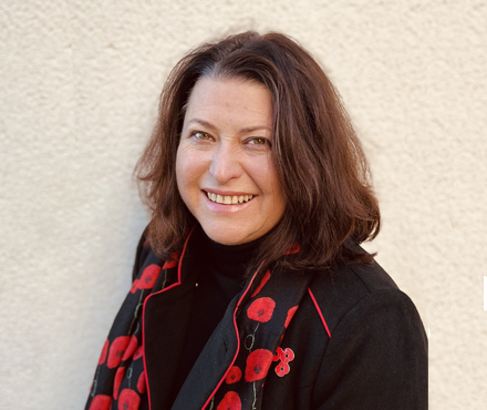 Sandie smiling whilst wearing poppy scarf and poppy.