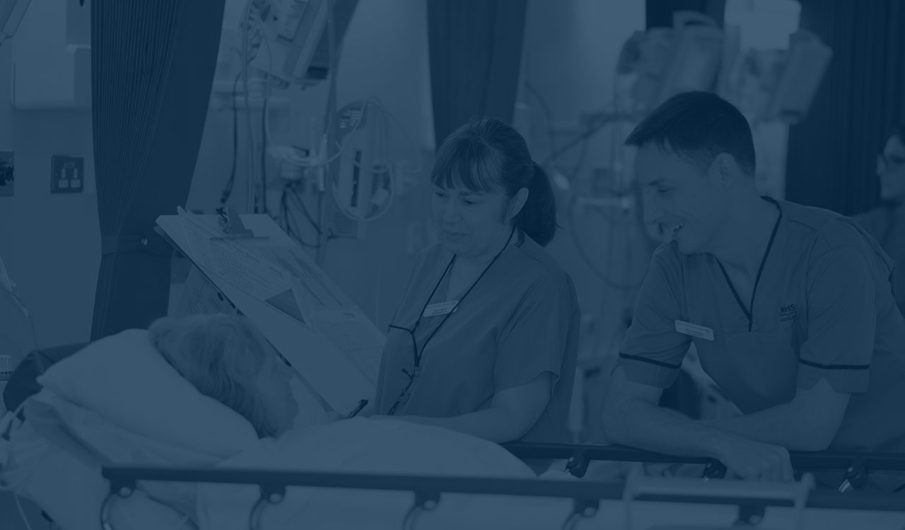 Male and female nurse speaking to woman patient in bed.