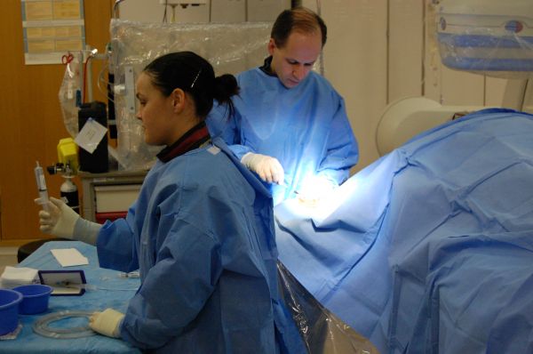 Surgeon working alongside female theatre staff who is holding a syringe. 